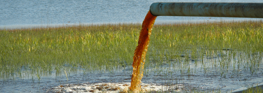pipe dumping orange water into a lake